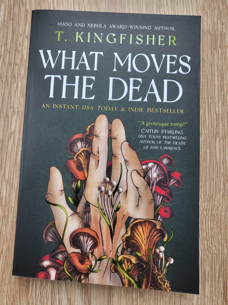 Photo of T. Kingfisher's What Moves the Dead book cover, featuring a hand splitting open with numerous mushrooms growing on and out of it.